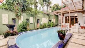 A swimming pool with blue mosaic tiles, surrounded by greenery and white outdoor furniture. - Capital O 90066 Tobana Pejaten House (Jakarta)