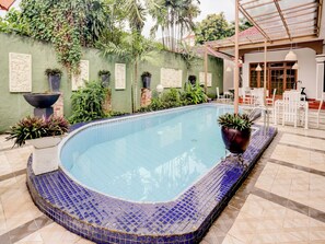 A swimming pool with blue mosaic tiles, surrounded by greenery and white outdoor furniture. - Capital O 90066 Tobana Pejaten House (Jakarta)
