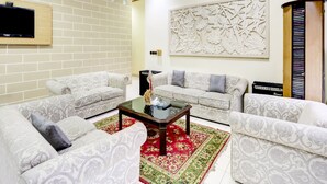A living room with two patterned sofas, a coffee table, a TV mounted on a brick wall, and a decorative wall piece. - Capital O 90066 Tobana Pejaten House (Jakarta)