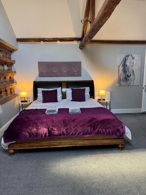 A bedroom with a large bed, wooden headboard, and a brick wall. - The Carriage House, Bilbrough, York. (York)