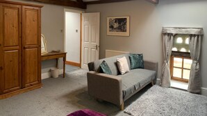 A cozy room with a wooden wardrobe, a sofa with patterned cushions, a small table, and a window with curtains.