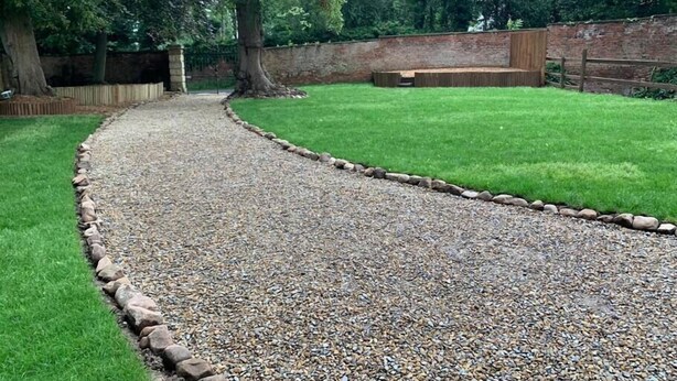 A gravel path leading through a grassy area with a brick wall and wooden fence in the background.