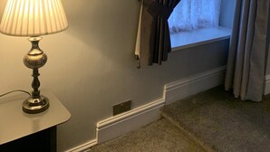 Une pièce avec une lampe sur une table, une fenêtre avec des rideaux et un sol recouvert d’une moquette.