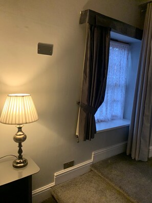 A room with a lamp on a table, a window with curtains, and a carpeted floor. - The Carriage House, Bilbrough, York. (York)