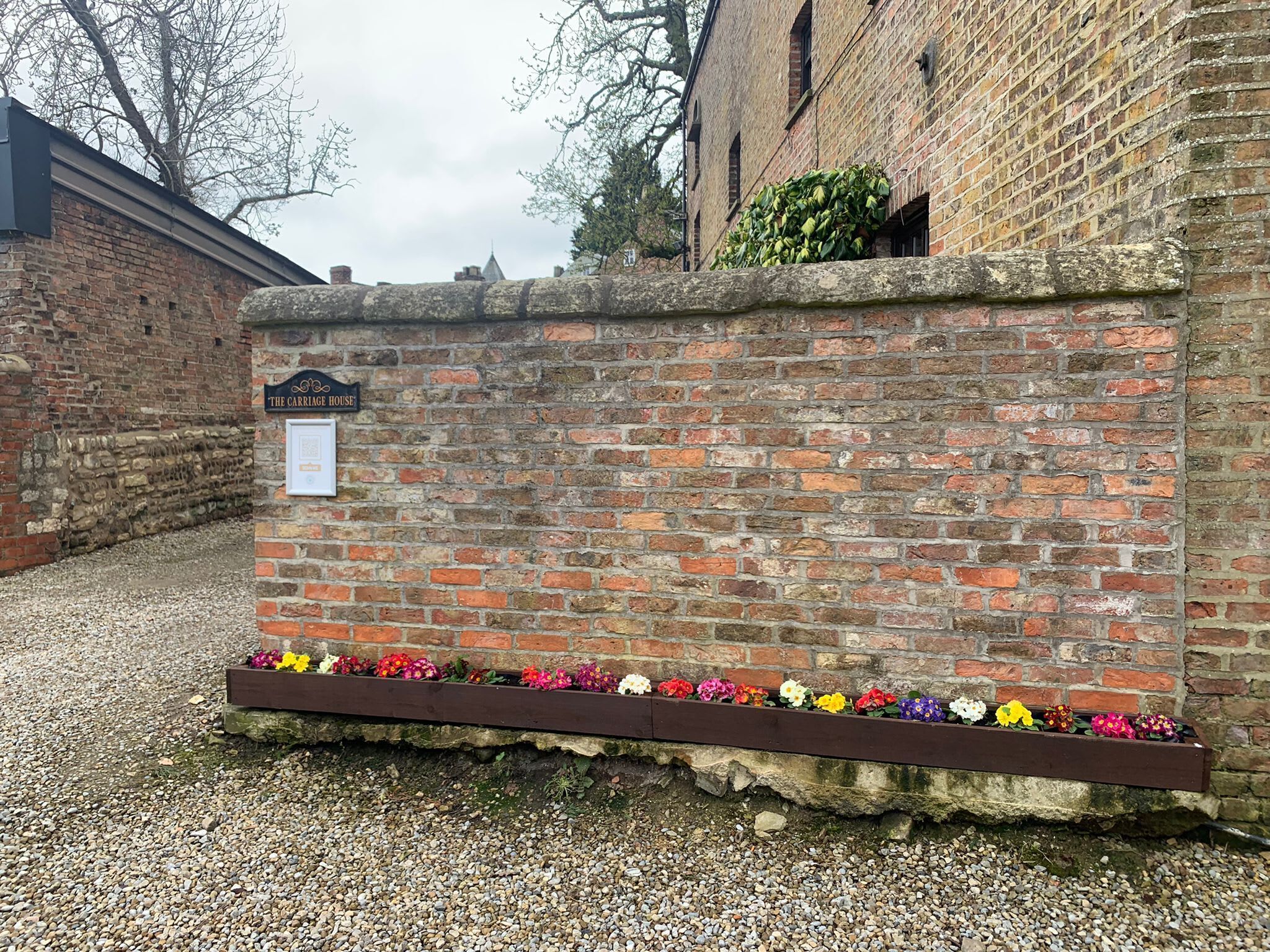 Un muro de ladrillo con un letrero que dice 'The Carriage House' y un macizo de flores variado.