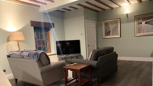 A living room with a sofa, a small table, a TV, and a window with blinds.