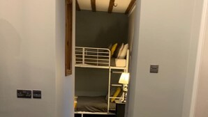 A narrow hallway leading to a room with a bunk bed, a lamp, and a carpeted floor.