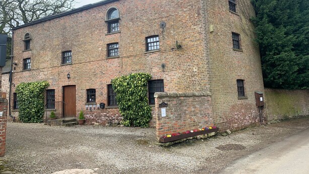 Un bâtiment en briques doté de nombreuses fenêtres et d’un petit jardin agrémenté de fleurs.