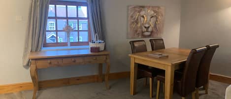 Un comedor con una mesa y sillas de madera, una ventana con cortinas, y un cuadro de un león en la pared.