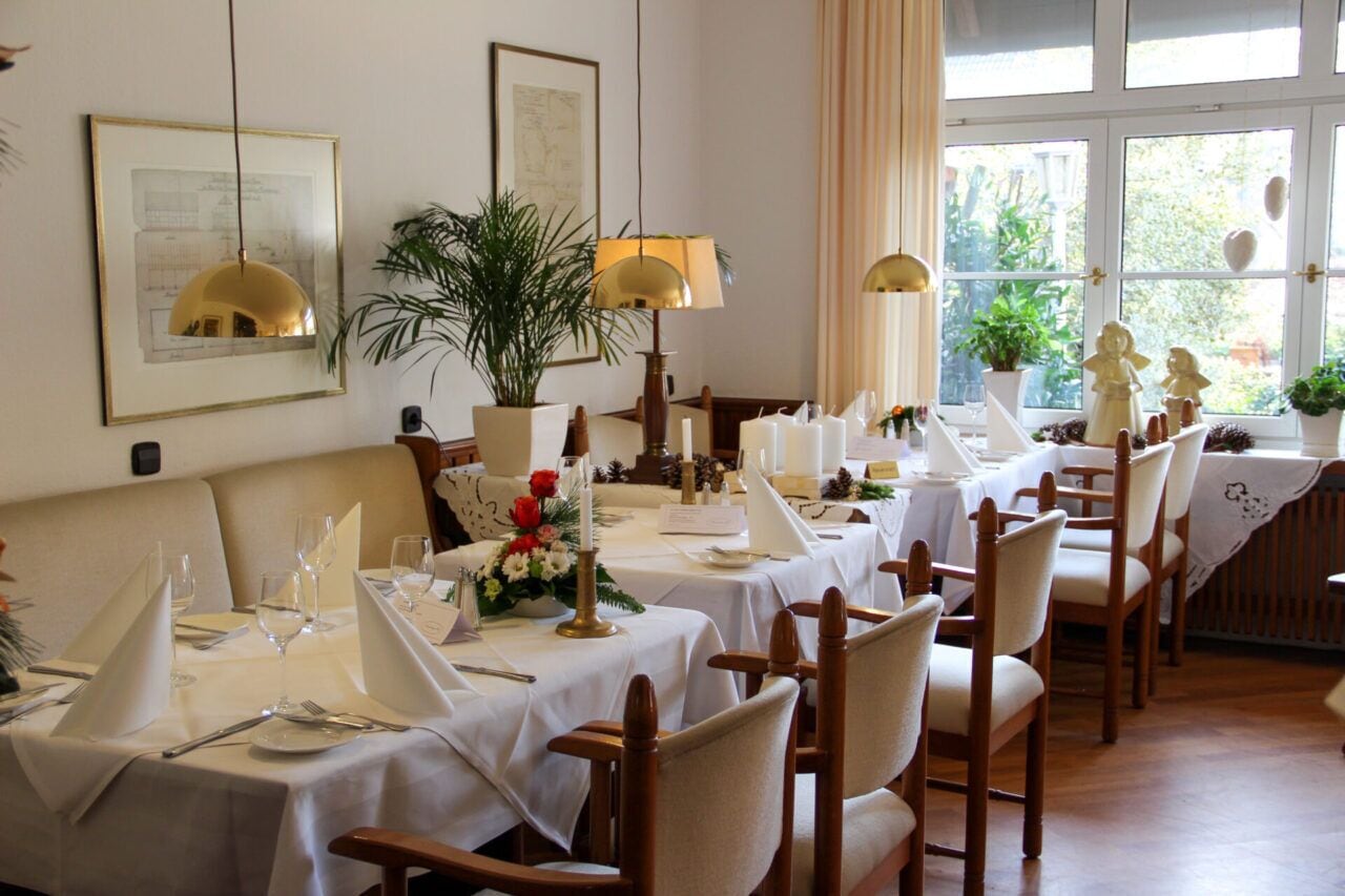 Un comedor con mesas dispuestas para comer, sillas, una planta en maceta y cuadros en las paredes.