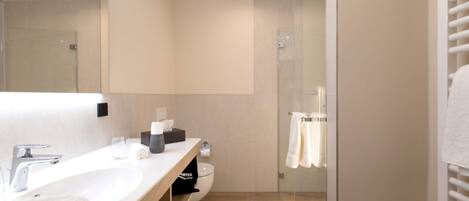 Un baño moderno con un espejo grande, un lavabo blanco, cabina de ducha de vidrio y un perchero para toallas.