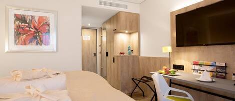 Una habitación de hotel con una cama, un escritorio, una silla, un televisor y un cuadro en la pared.