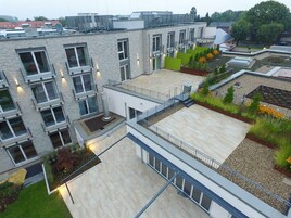 Um edifício moderno com várias varandas, um jardim no terraço e um terraço plano.