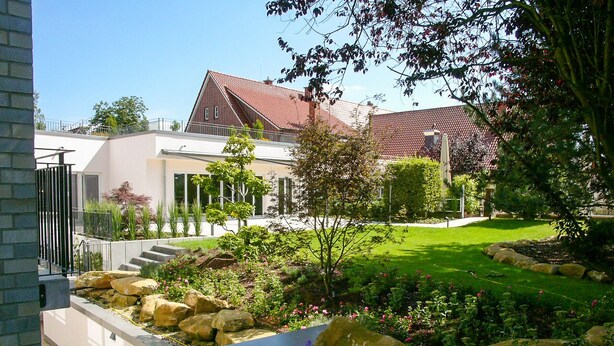 Une maison moderne dotée d’un jardin bien entretenu, d’un chemin en pierre et d’un toit recouvert de tuiles rouges.
