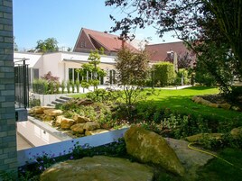 Uma casa moderna com um jardim bem cuidado, um caminho de pedra e um telhado de telhas vermelhas.