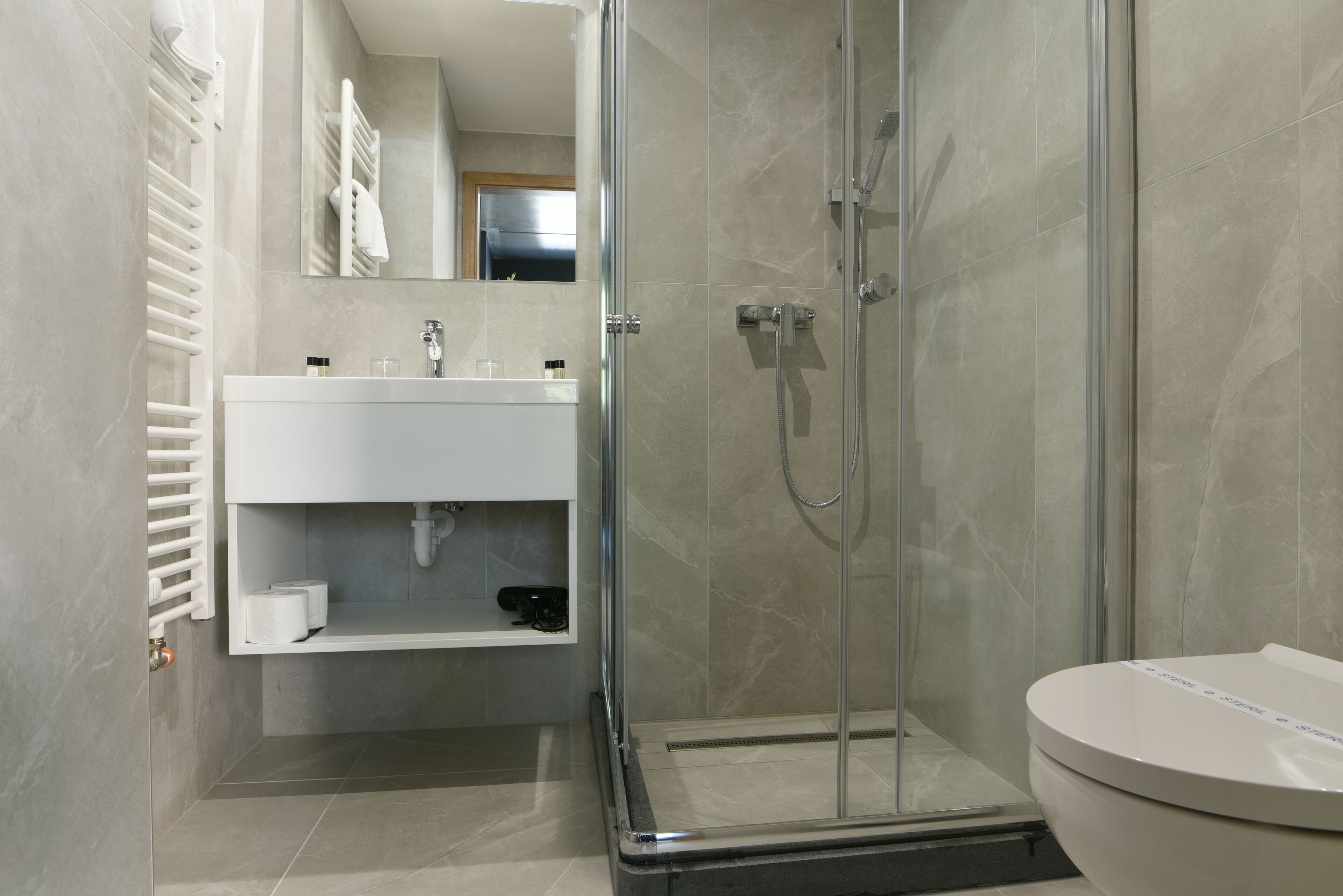 A modern bathroom with a glass-enclosed shower, a white sink, and a toilet.
