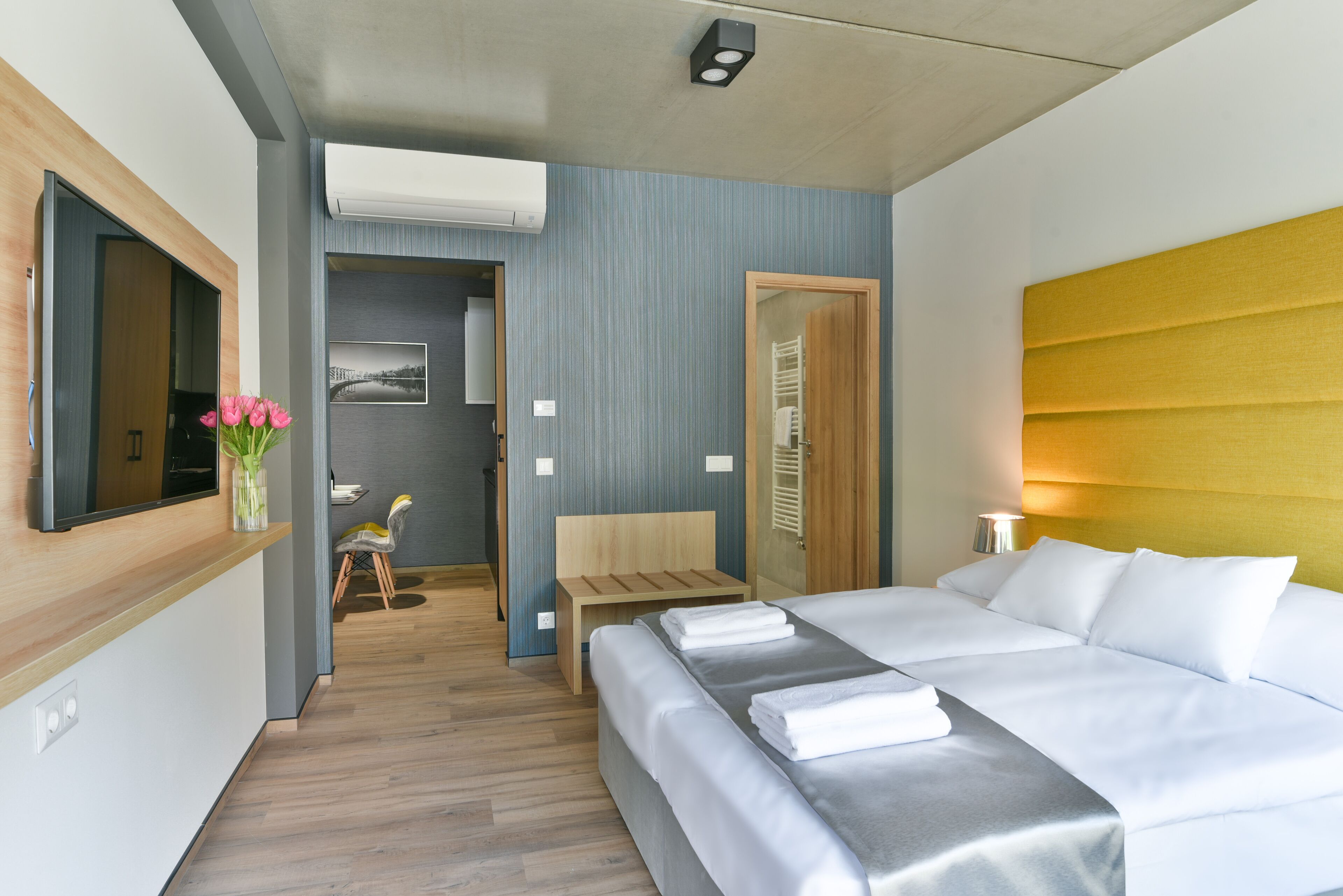 Une chambre d’hôtel moderne avec un grand lit, une table de chevet, un miroir et une tête de lit en bois.
