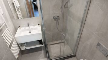 A modern bathroom with a glass-enclosed shower, a white sink, and a mirror.