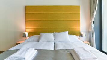A hotel room with a large bed, two bedside tables, a headboard, and a window with curtains.