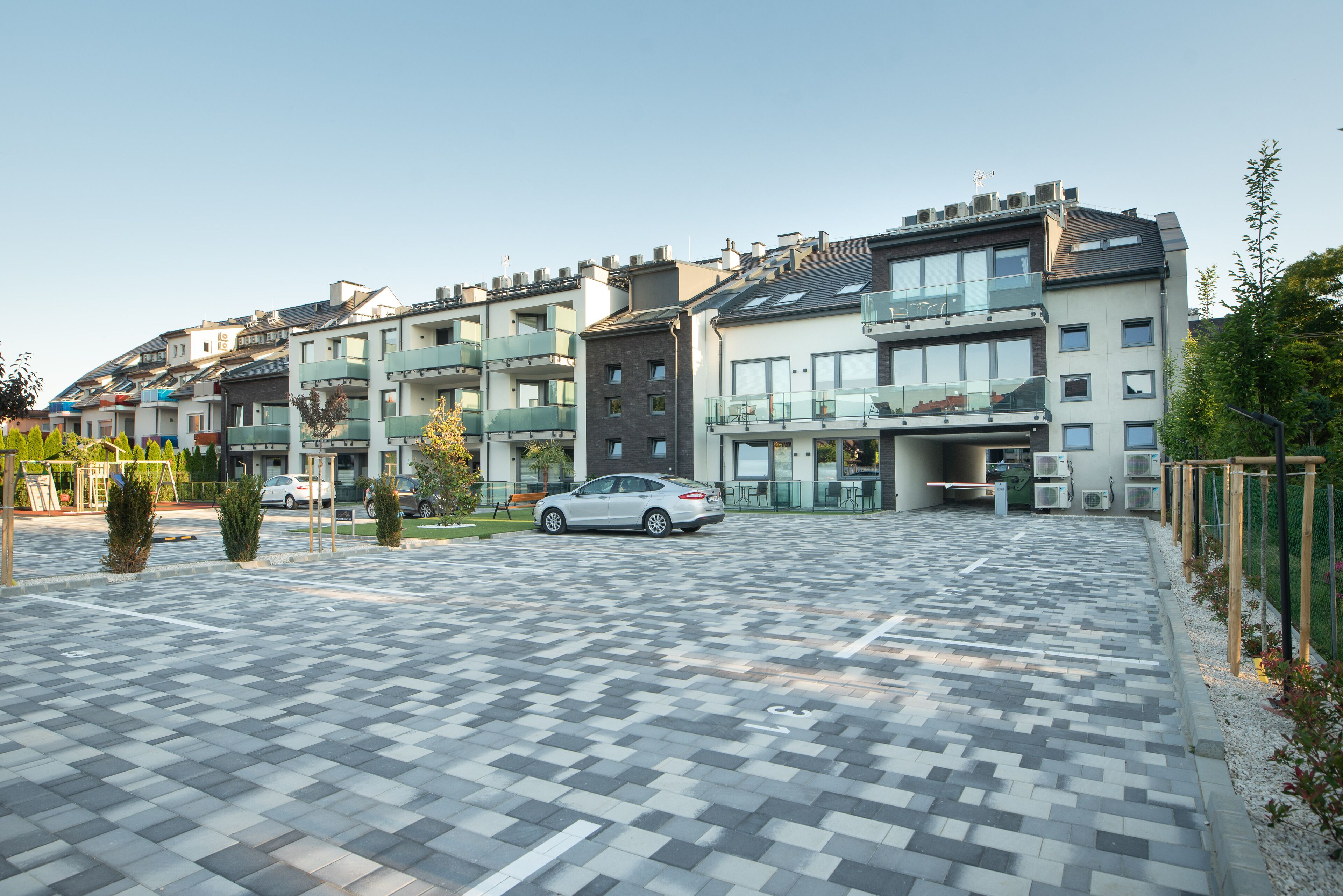 A modern apartment building with multiple balconies, a parking area, and a small garden.