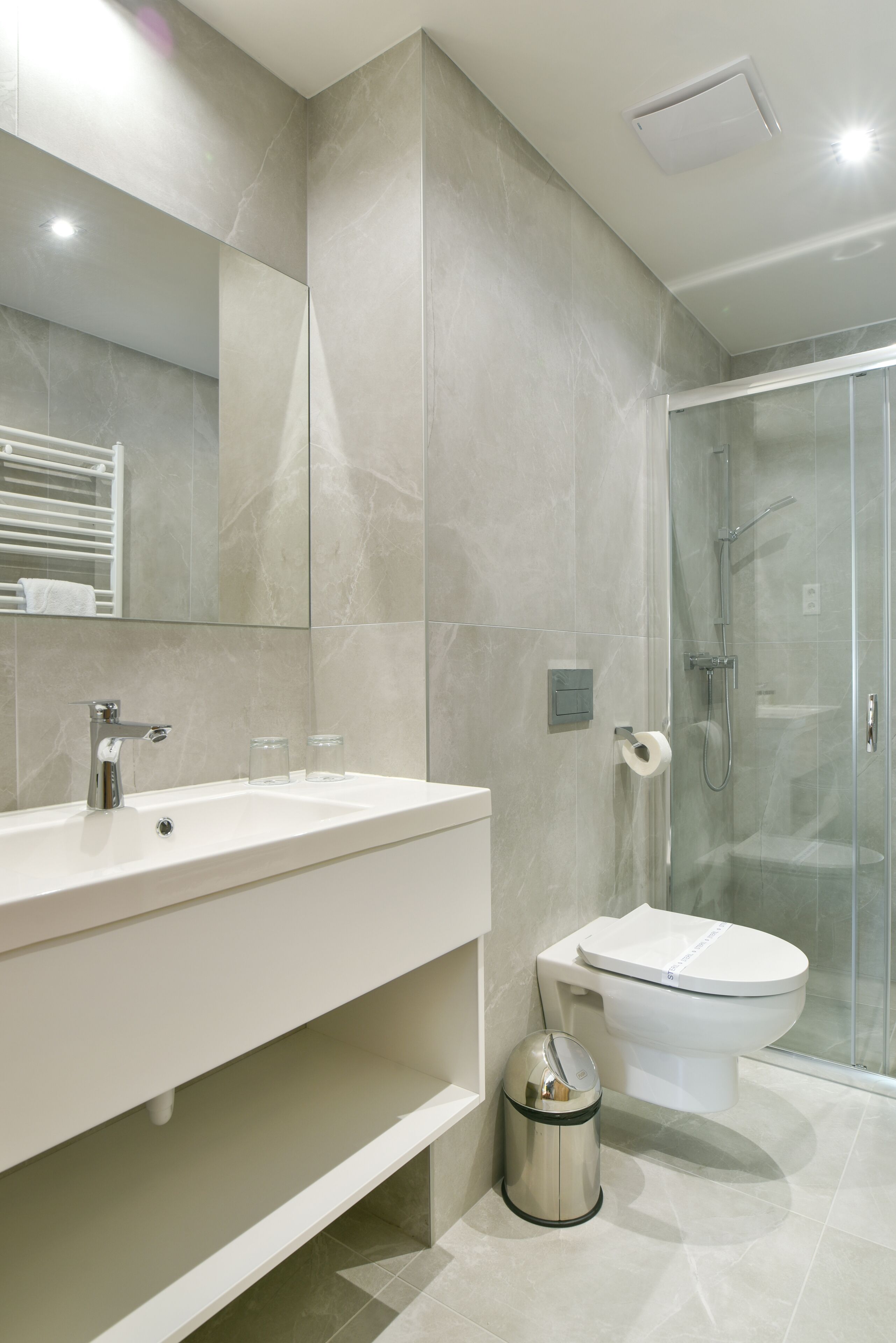 A modern bathroom with a large mirror, a sink, a toilet, and a glass-enclosed shower.