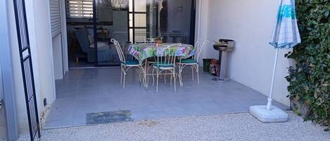 Un patio con mesa y sillas, un pequeño jardín y un ventanal corredera que da a un espacio interior.