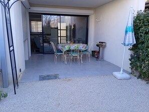 Un patio con mesa y sillas, un pequeño jardín y un ventanal corredera que da a un espacio interior.