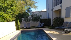 Une piscine rectangulaire à l’eau d’un bleu limpide, entourée d’une terrasse en béton. On y trouve des chaises longues et une petite table.