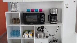 Une cuisine avec des meubles blancs, un four à micro-ondes, une machine à café et divers ustensiles de cuisine.