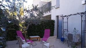 Un espace extérieur aménagé avec deux chaises et une table, entouré de gravier et de verdure.