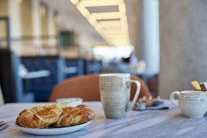 Een tafel met croissants, een mok en een kopje, waarschijnlijk in een café.
