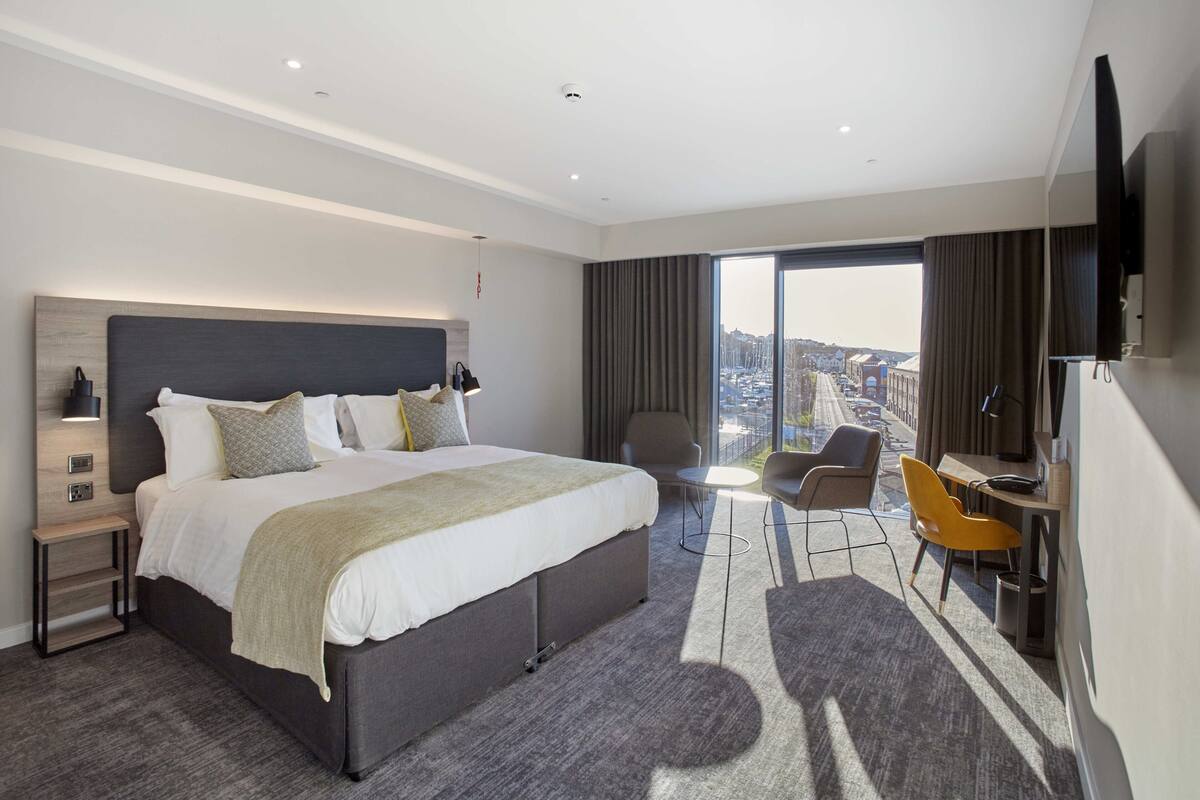 Ein modernes Hotelzimmer mit einem großen Bett, einem Schreibtisch, einem Sessel und einem Fernseher.