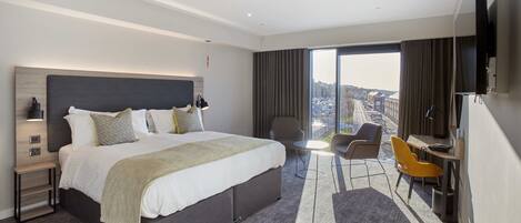 Una habitación de hotel moderna con una cama grande, un escritorio, una silla y un televisor.