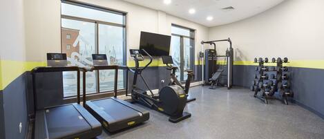 A gym with treadmills, an elliptical, a weight rack, and a TV screen.