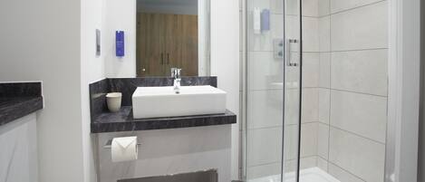 Une salle de bain moderne avec un lavabo blanc, un plan de toilette en marbre et une cabine de douche en verre.