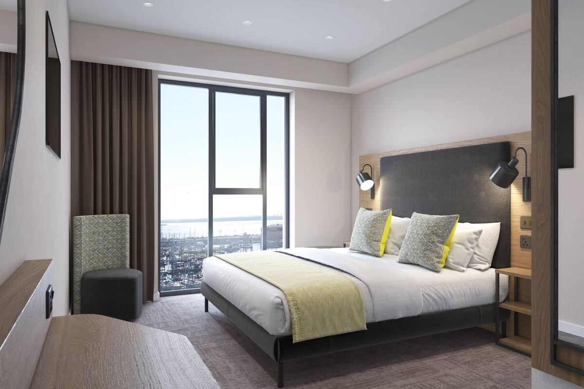 Ein modernes Hotelzimmer mit einem großen Bett, Blick auf die Stadt und einem Schreibtisch mit Stuhl.