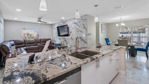 A modern kitchen with a marble countertop, a built-in dishwasher, and a dining area with a blue chair and a table. - 8 minutes from the AIRPORT~ New SaL POOL - WiFi 1gbps/free Parking... BBQ (Tampa)