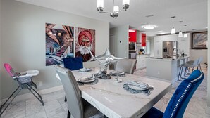 A dining area with a marble table, chairs, and a chandelier. There is a kitchen in the background with modern appliances and a red accent wall. - 8 minutes from the AIRPORT~ New SaL POOL - WiFi 1gbps/free Parking... BBQ (Tampa)