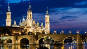 A historic building with multiple domes and towers, a stone bridge with arches, and a river reflecting the structure. - Modern apartment in the historic center !!! (Zaragoza)