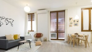 A modern living room with a grey sofa, a coffee table, a wicker chair, and a dining area with a wooden table and chairs. - Modern apartment in the historic center !!! (Zaragoza)
