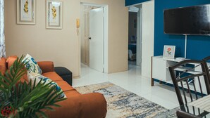 Un salon comprenant un canapé, une table basse, un téléviseur et une porte donnant sur une autre pièce.