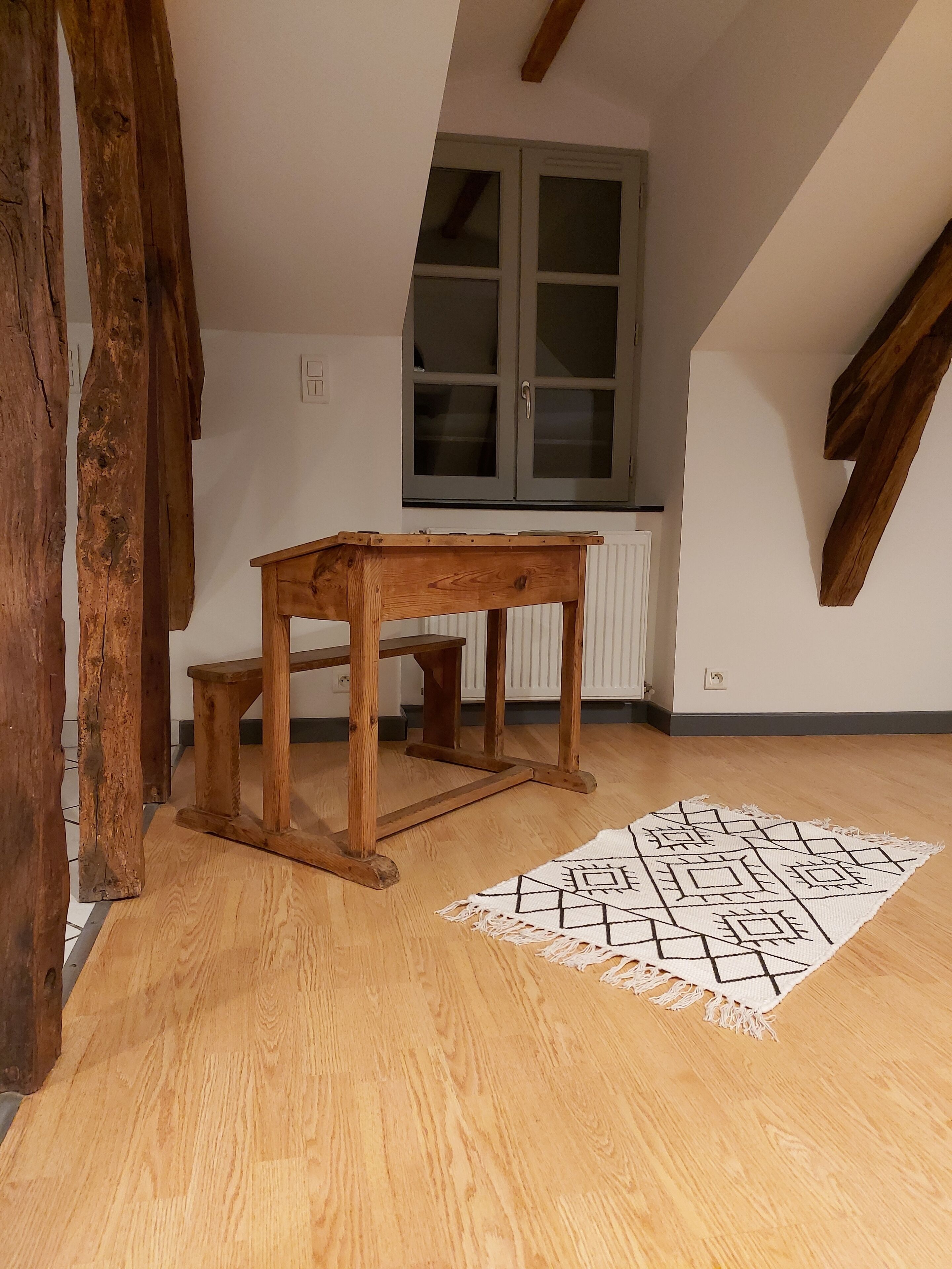 Ein Zimmer mit einem Holztisch, einem gemusterten Teppich und einem Fenster mit einem Schrank.