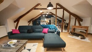 Ett mysigt vardagsrum i loftstil med en hörnsoffa, ett soffbord i trä och en hund som vilar på golvet.
