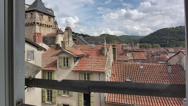 En vy över en stadsbild genom ett fönster, med en blandning av traditionella och moderna byggnader, röda tegeltak och ett framträdande torn.