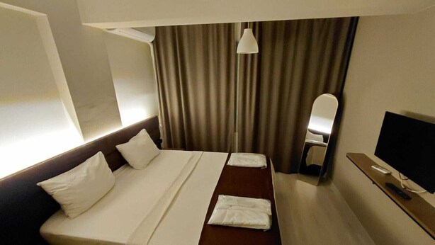 A hotel room with a bed, bedside table, TV, and curtains.