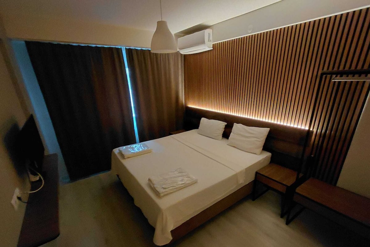 A hotel room with a large bed, bedside tables, a desk, and a modern headboard.