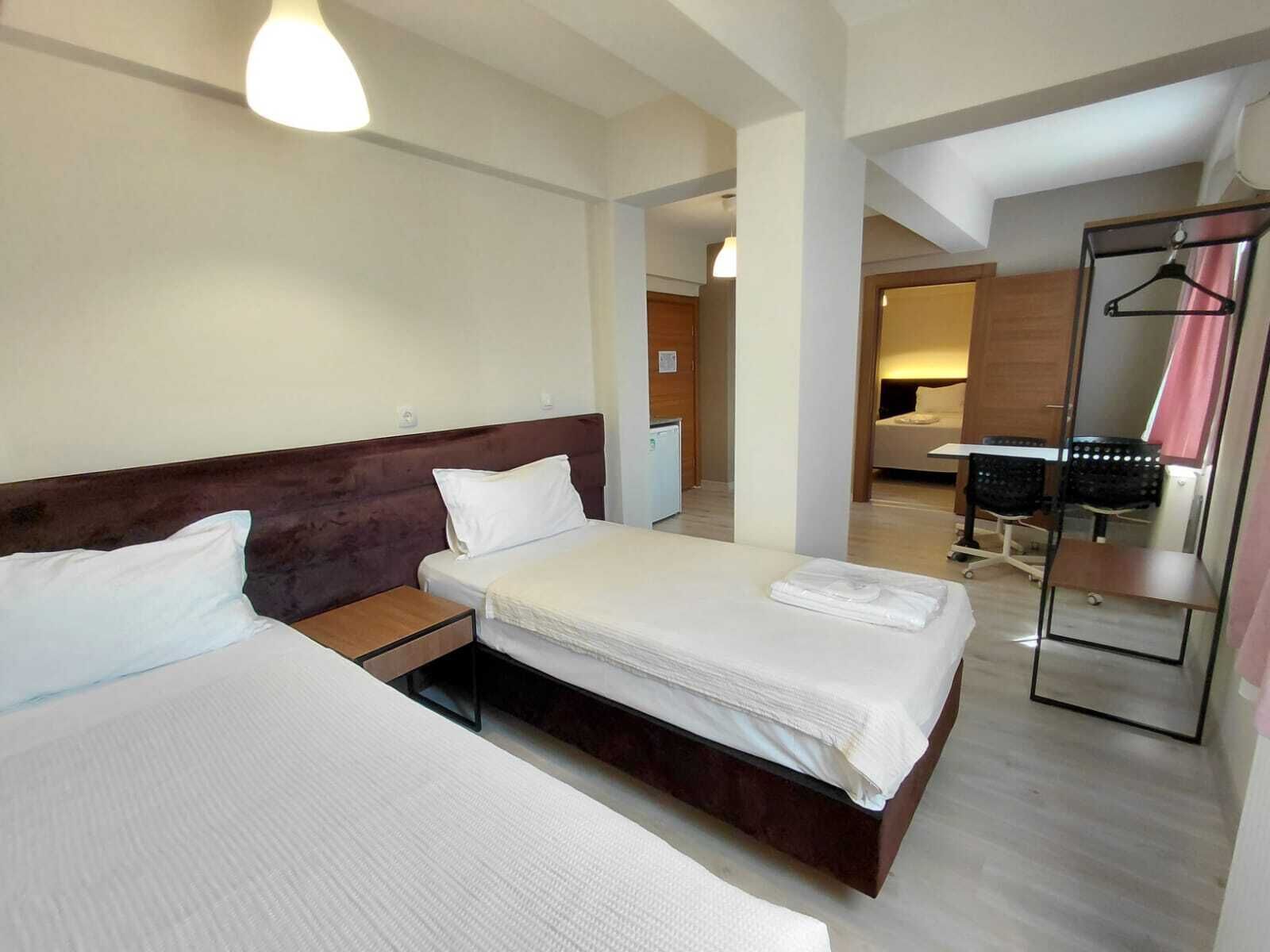 A hotel room with two beds, a desk, a chair, a mirror, and a wardrobe.