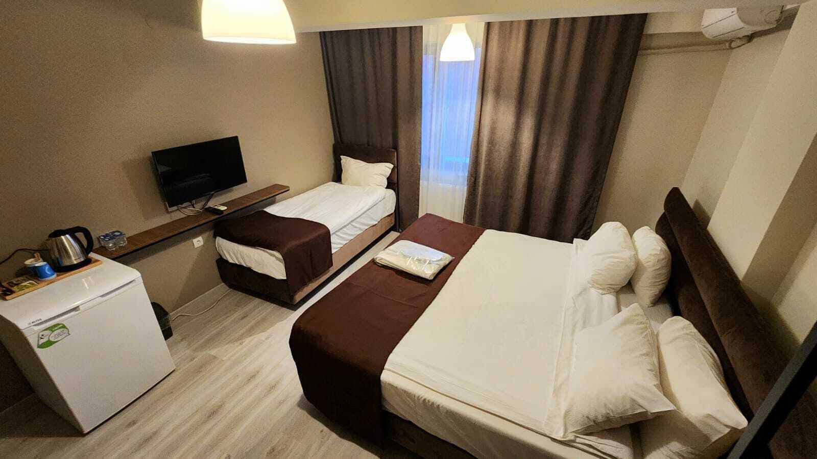 Habitación de hotel con dos camas, televisión, refrigerador pequeño y ventana con cortinas.