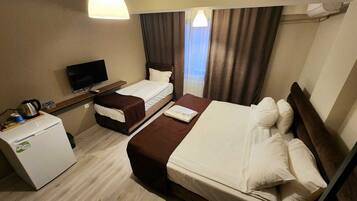 Habitación de hotel con dos camas, televisión, refrigerador pequeño y ventana con cortinas.