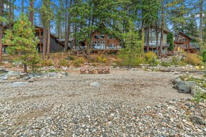 A cabin with a deck, surrounded by trees and a gravel path.